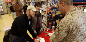 Man signing book at military event table.