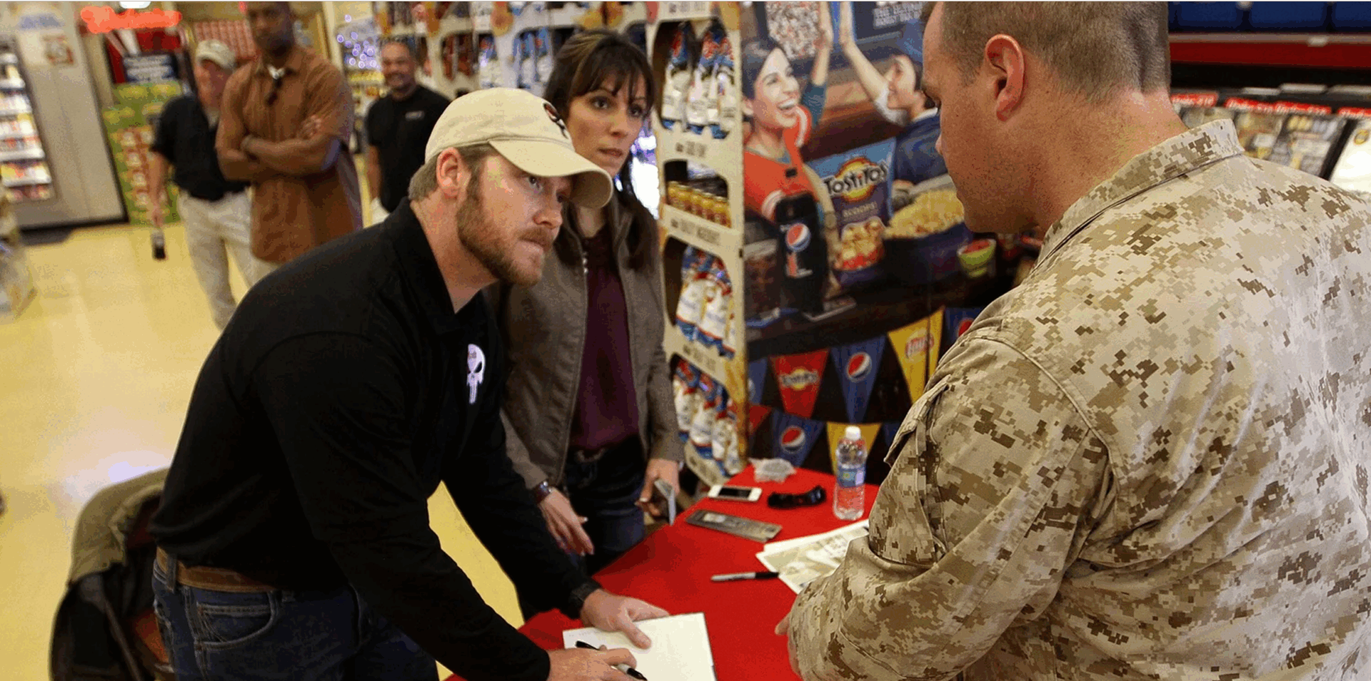 Man signing book at military event table.